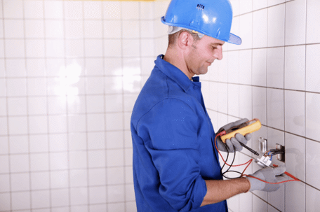 Man in blue hardhat repairing bathroom wiring