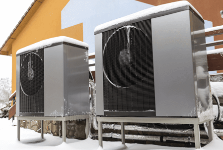 Two identical heat pumps covered with snow