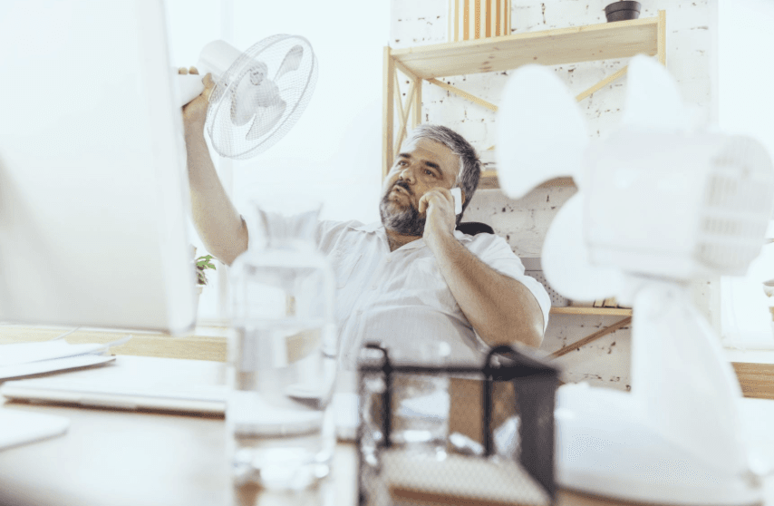 Man seated at desk holding fan above his head