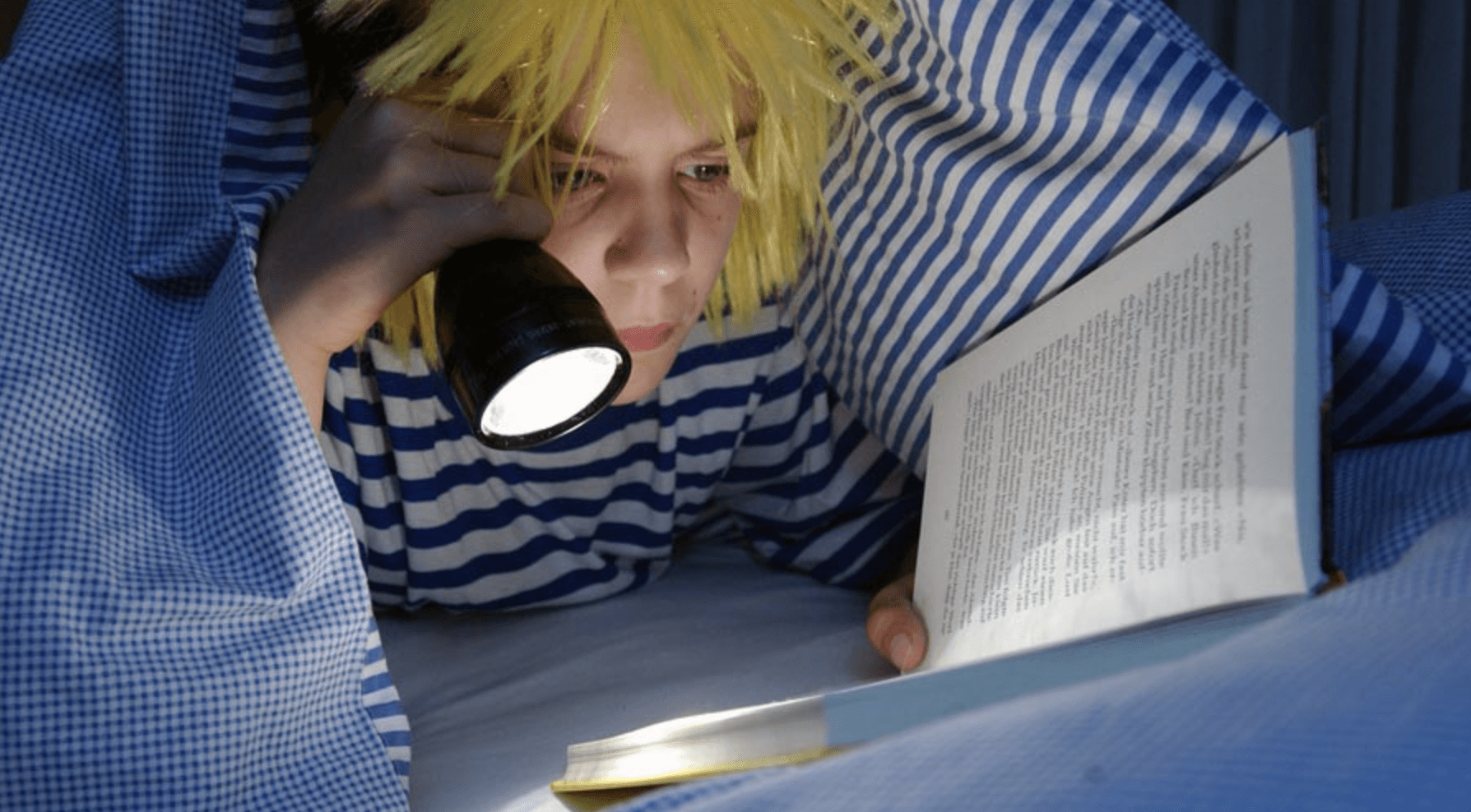 Boy reading under a blanket with a flashlight